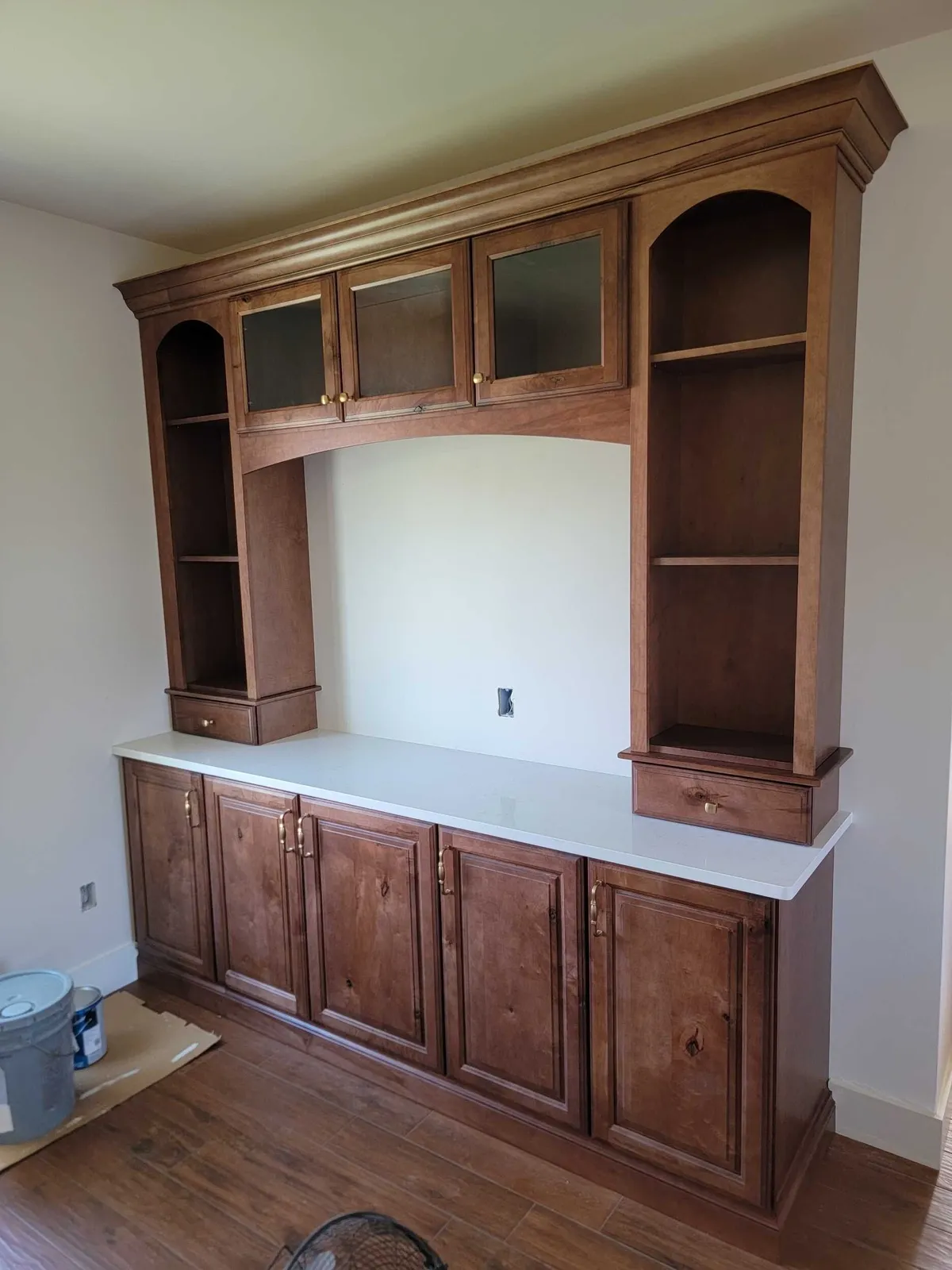 Built-in wood cabinetry with glass-front upper doors, arched open shelves, and a white countertop.