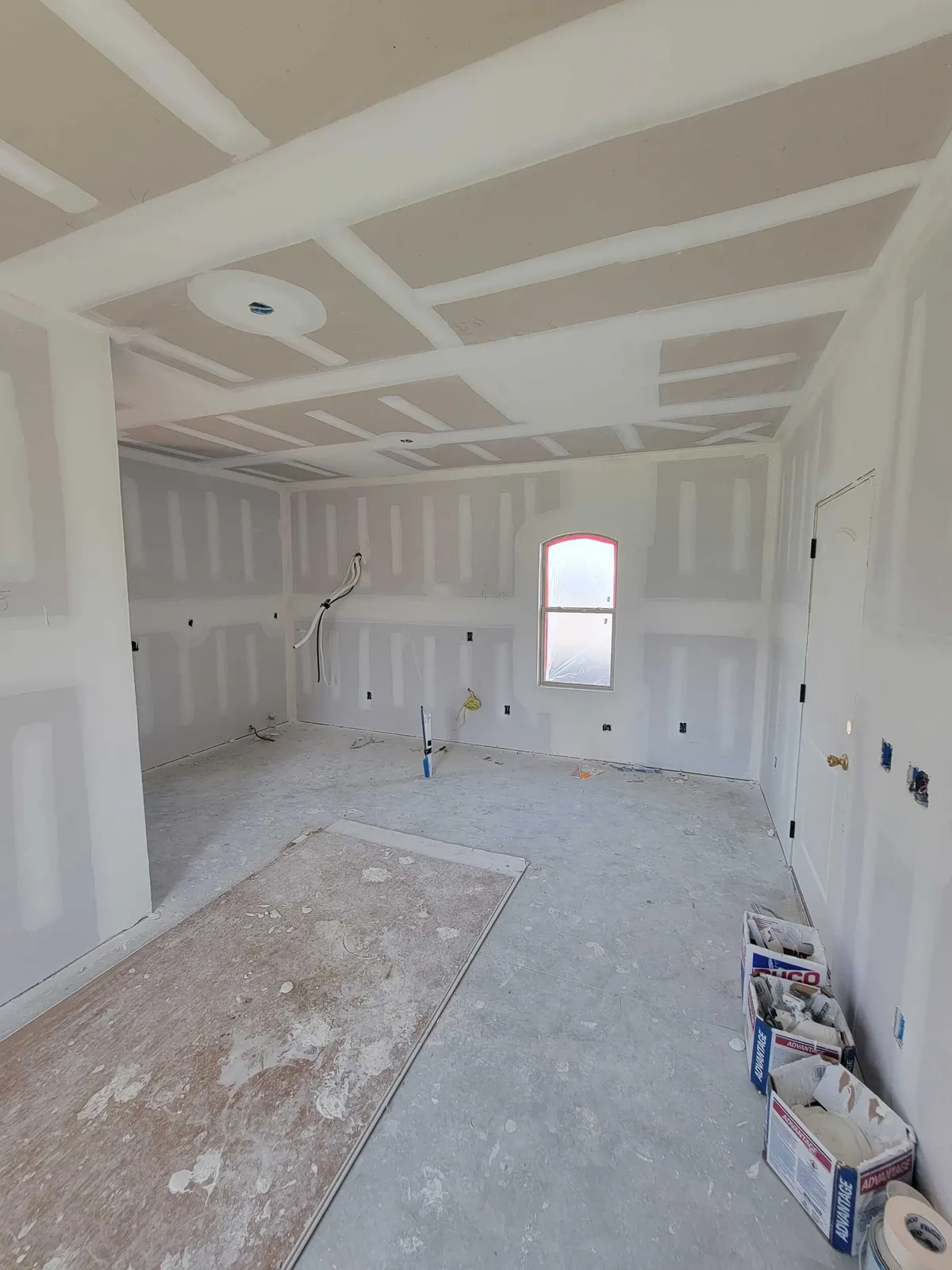 Main studio room with taped drywall on the walls and ceiling, an arched window at the far end, and supplies on the floor.