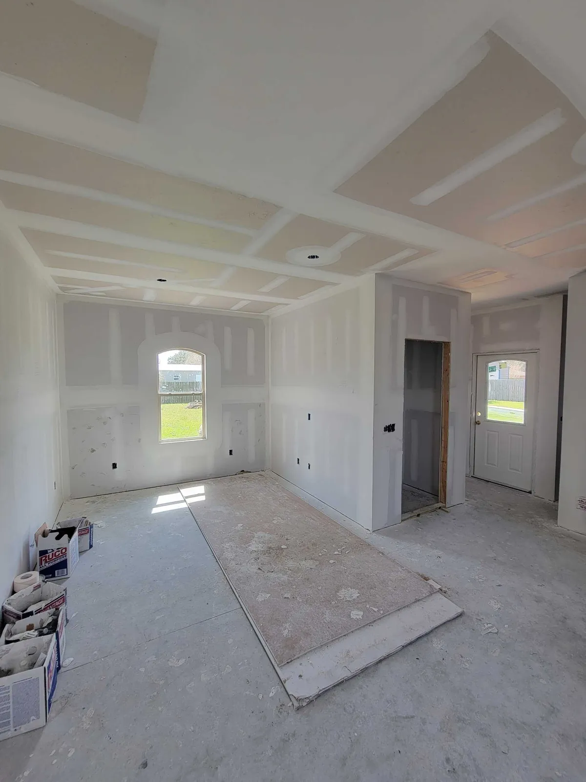 Taped drywall throughout the main room, looking toward an arched window and the back door.