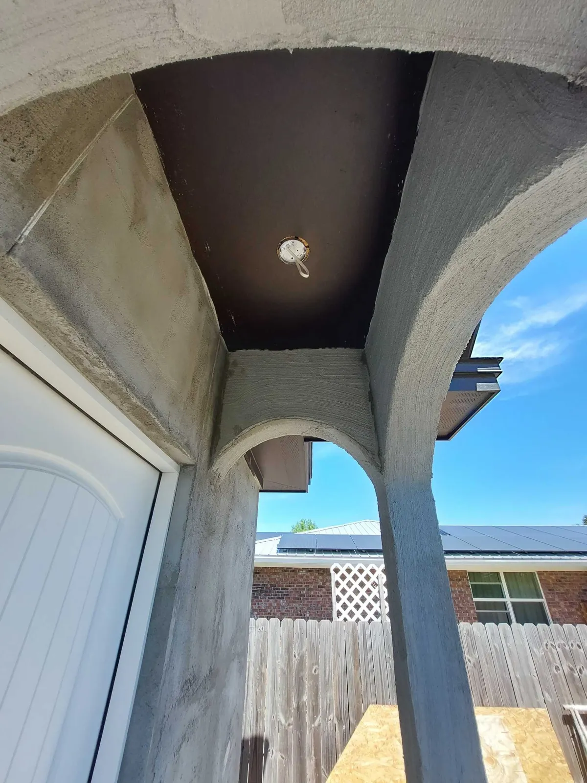Close view of stuccoed arches and a column at a porch corner, beside a white door.