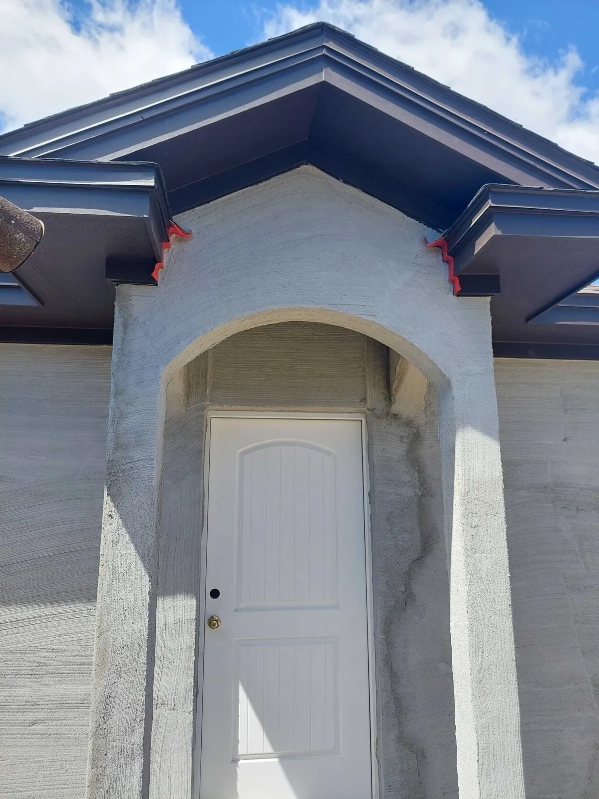 Entry arch and walls with a rough first coat of stucco, below the gable returns and dark fascia.