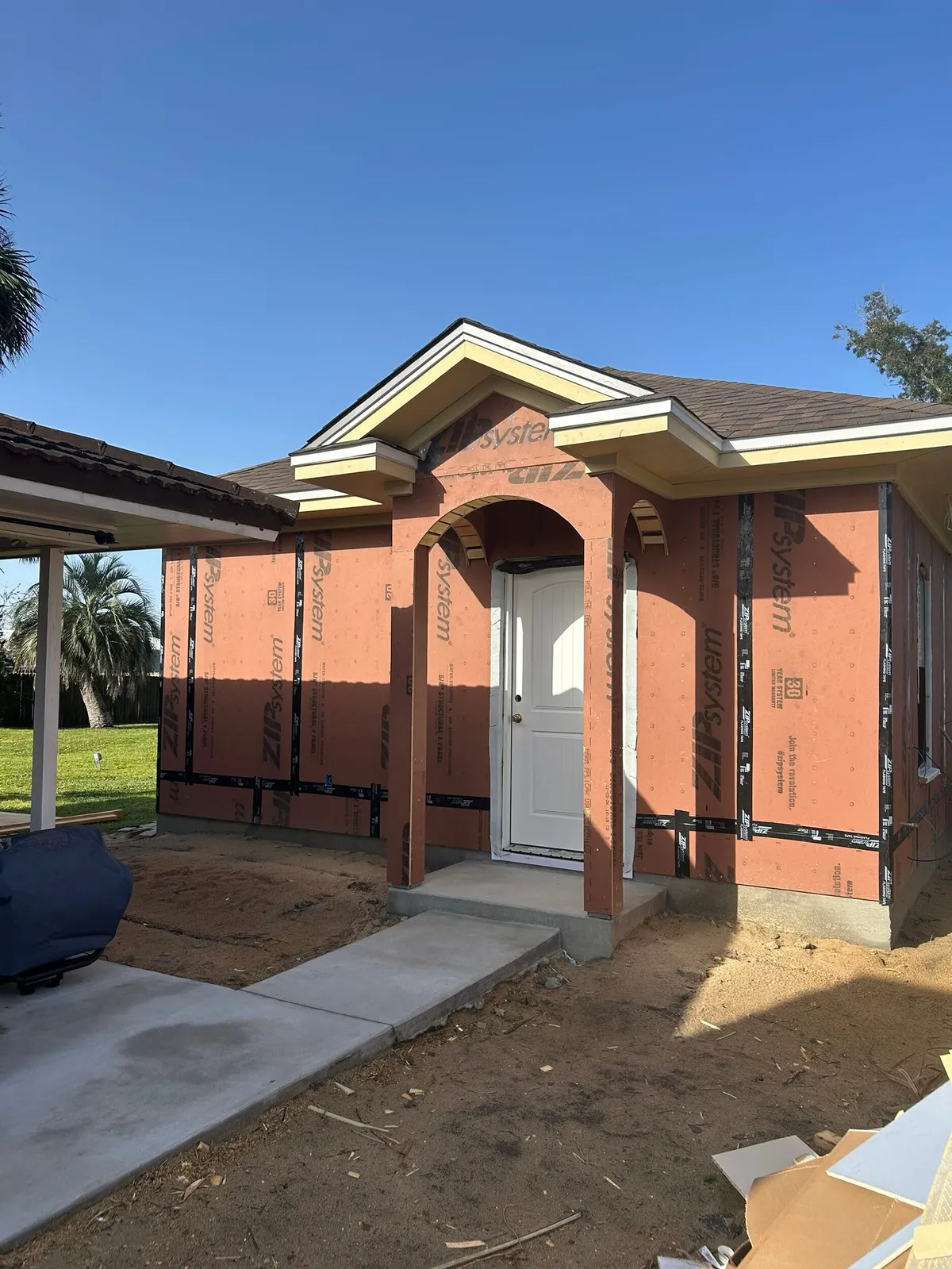 Sheathed studio entry with its arch, gable returns, and a white door, with a new concrete walk in front.