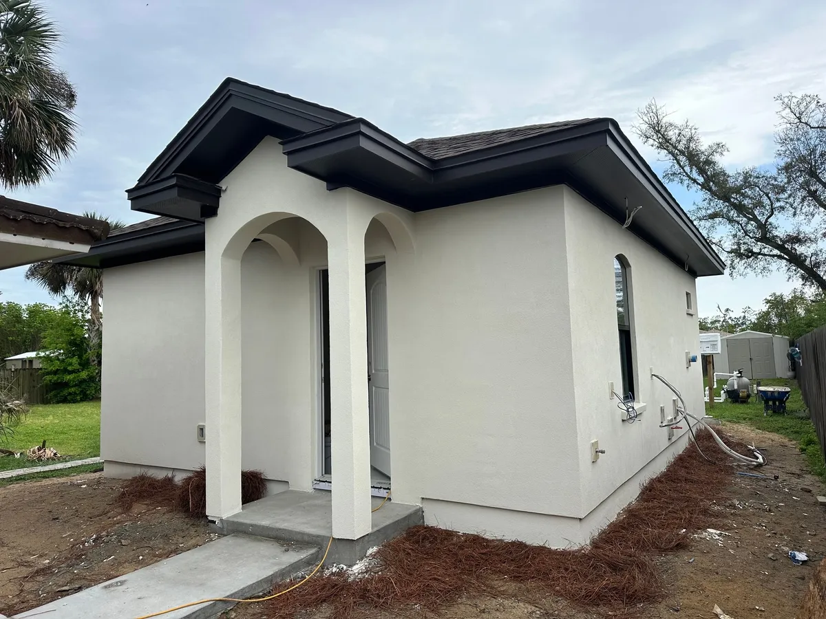 Angled view of the arched entry and gable returns, with a recessed window on the side wall, pine straw, and site work still in progress.