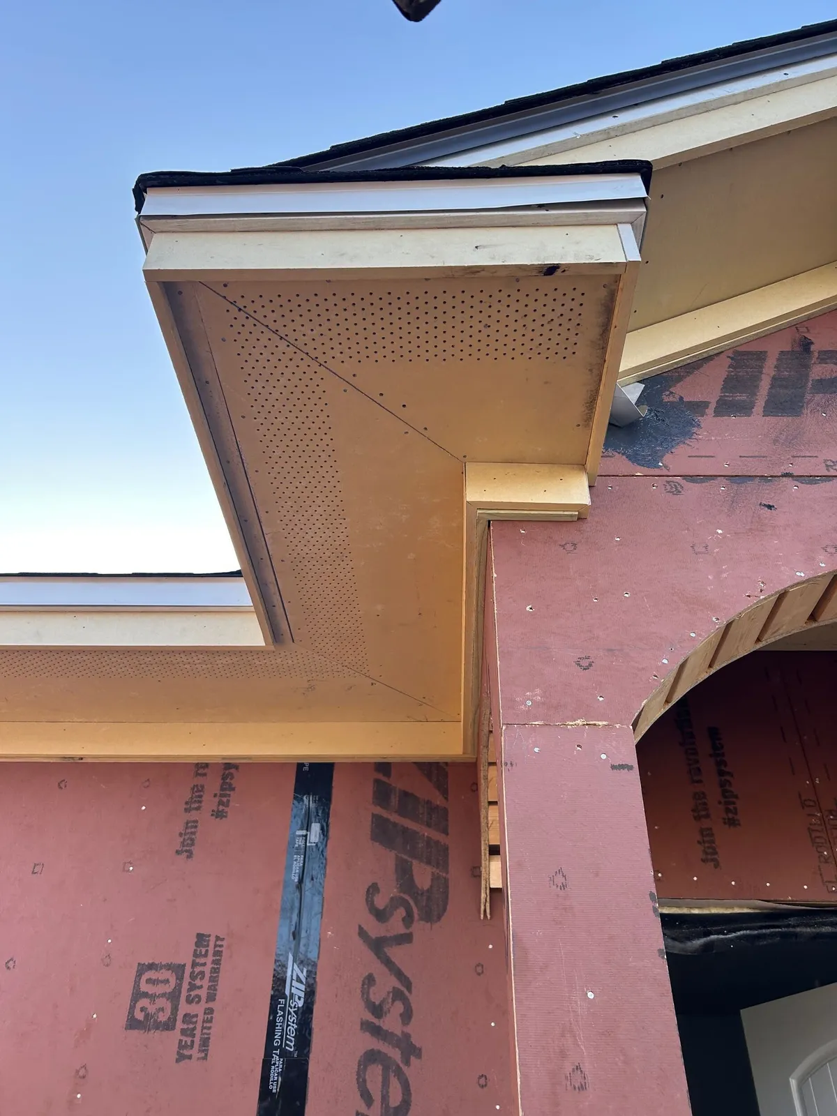 Close view of a gable return and soffit where the entry roof meets the main eave, above a framed arch.