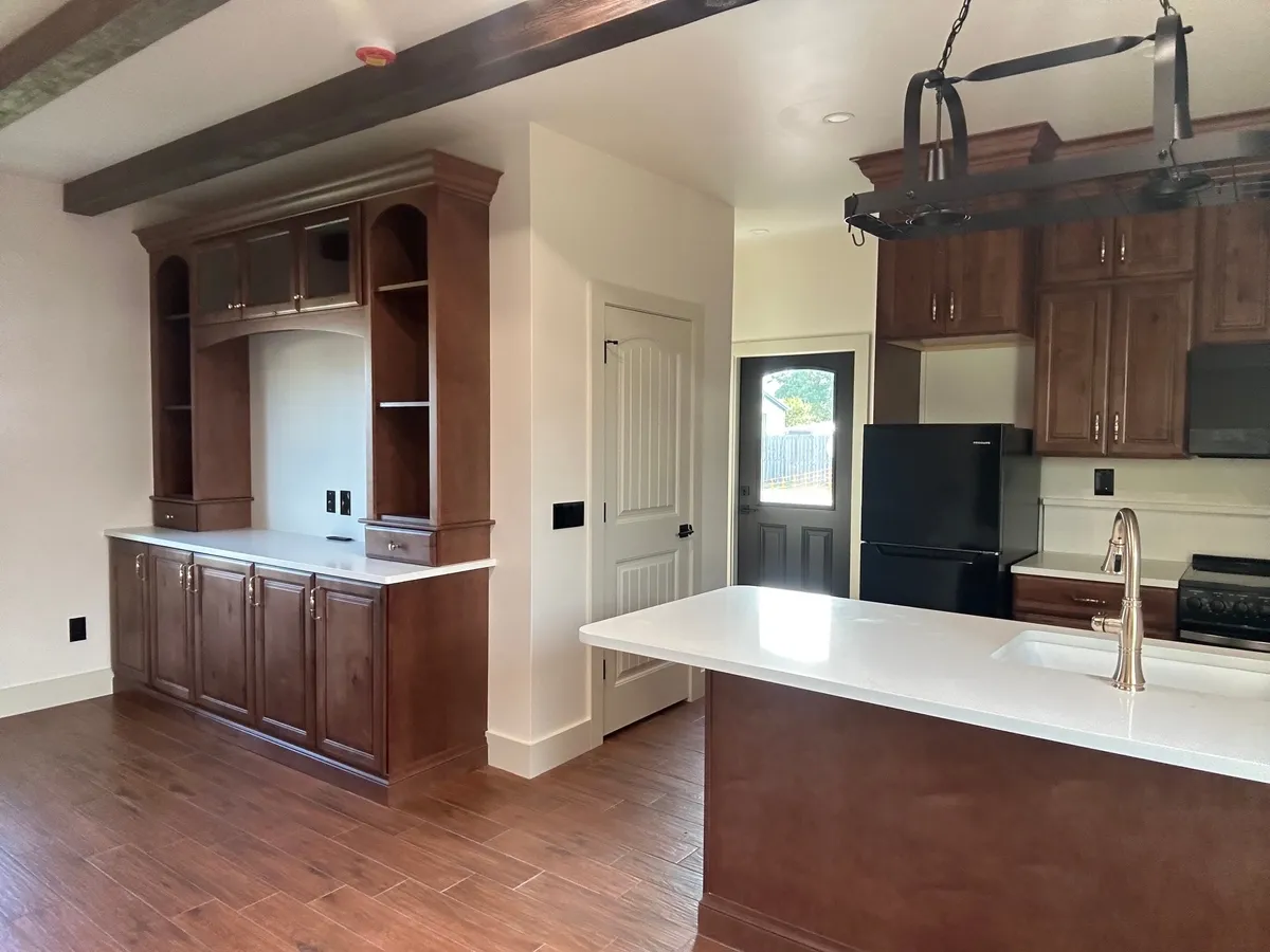 Wood hutch with glass-front upper doors and open arched shelves beside a white peninsula counter, a black refrigerator, and a back door with a window.