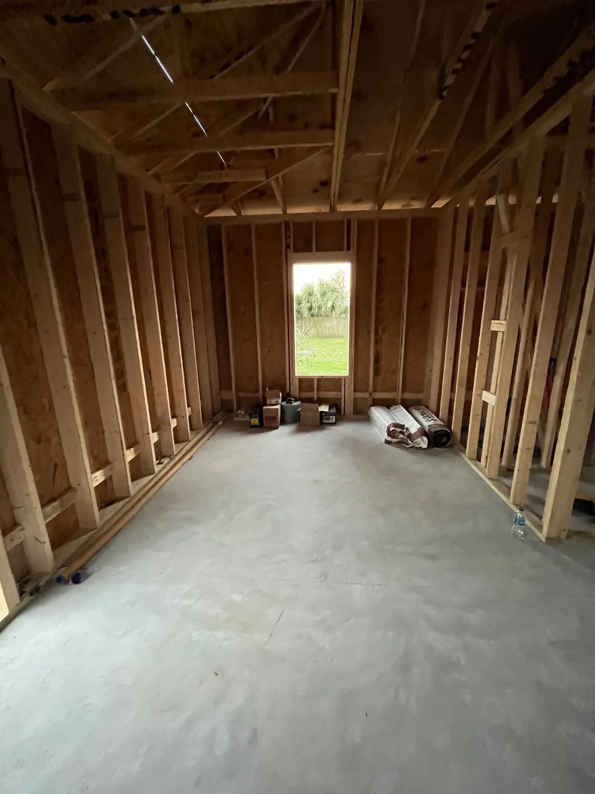 Interior wall and ceiling framing over the concrete slab, looking toward a tall window opening in the end wall.
