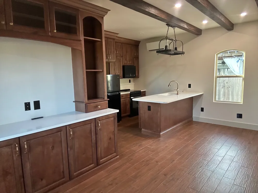 Studio kitchen with a tall wood hutch, dark ceiling beams, a hanging pot rack, a peninsula sink, and an arched window.