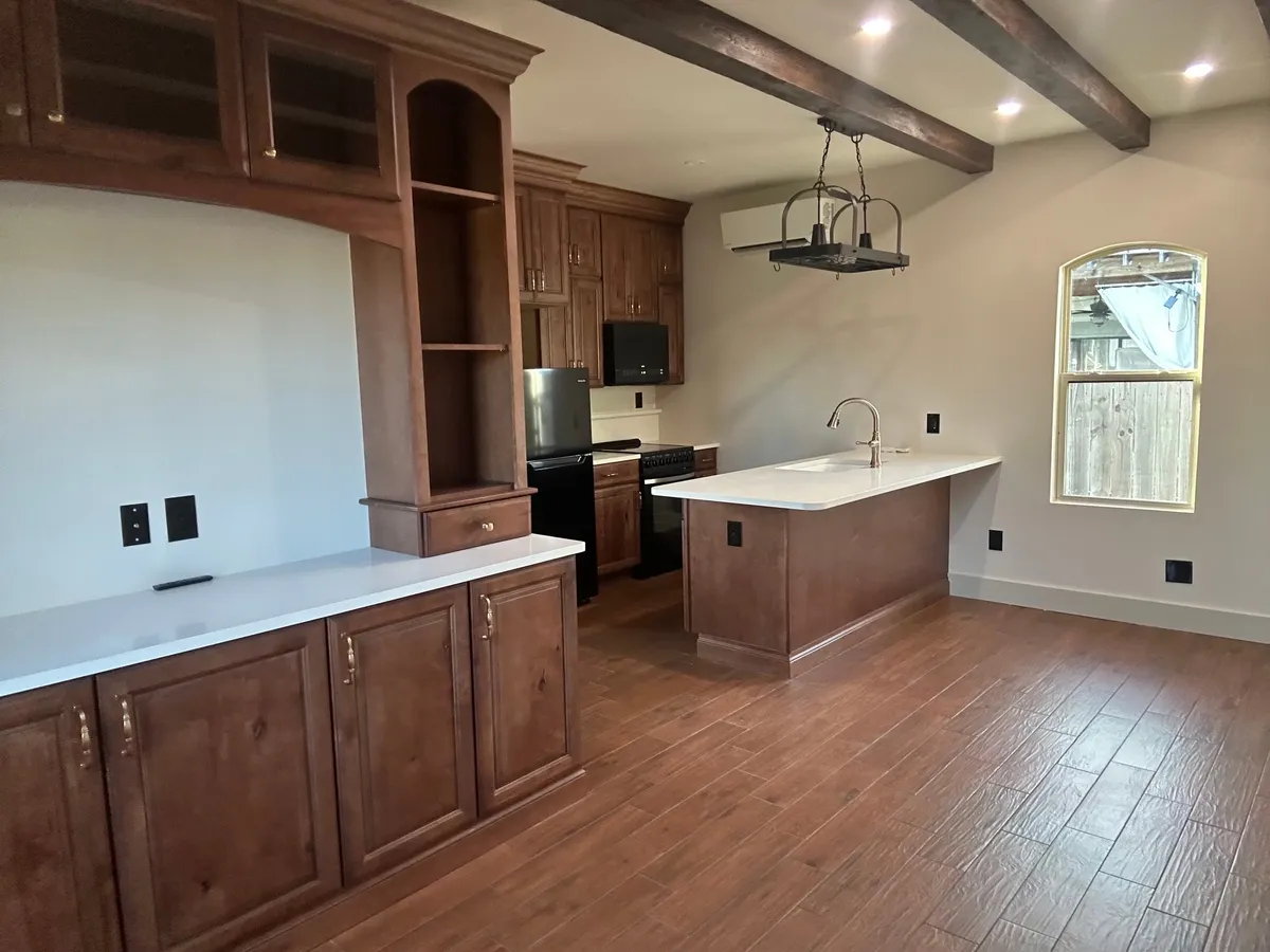 Studio kitchen with a tall wood hutch, dark ceiling beams, a hanging pot rack, a peninsula sink, and an arched window.