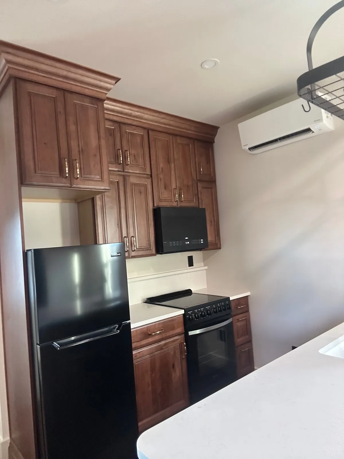 Wood kitchen cabinets, a black refrigerator, and a range, with a wall-mounted air conditioning unit near the ceiling.