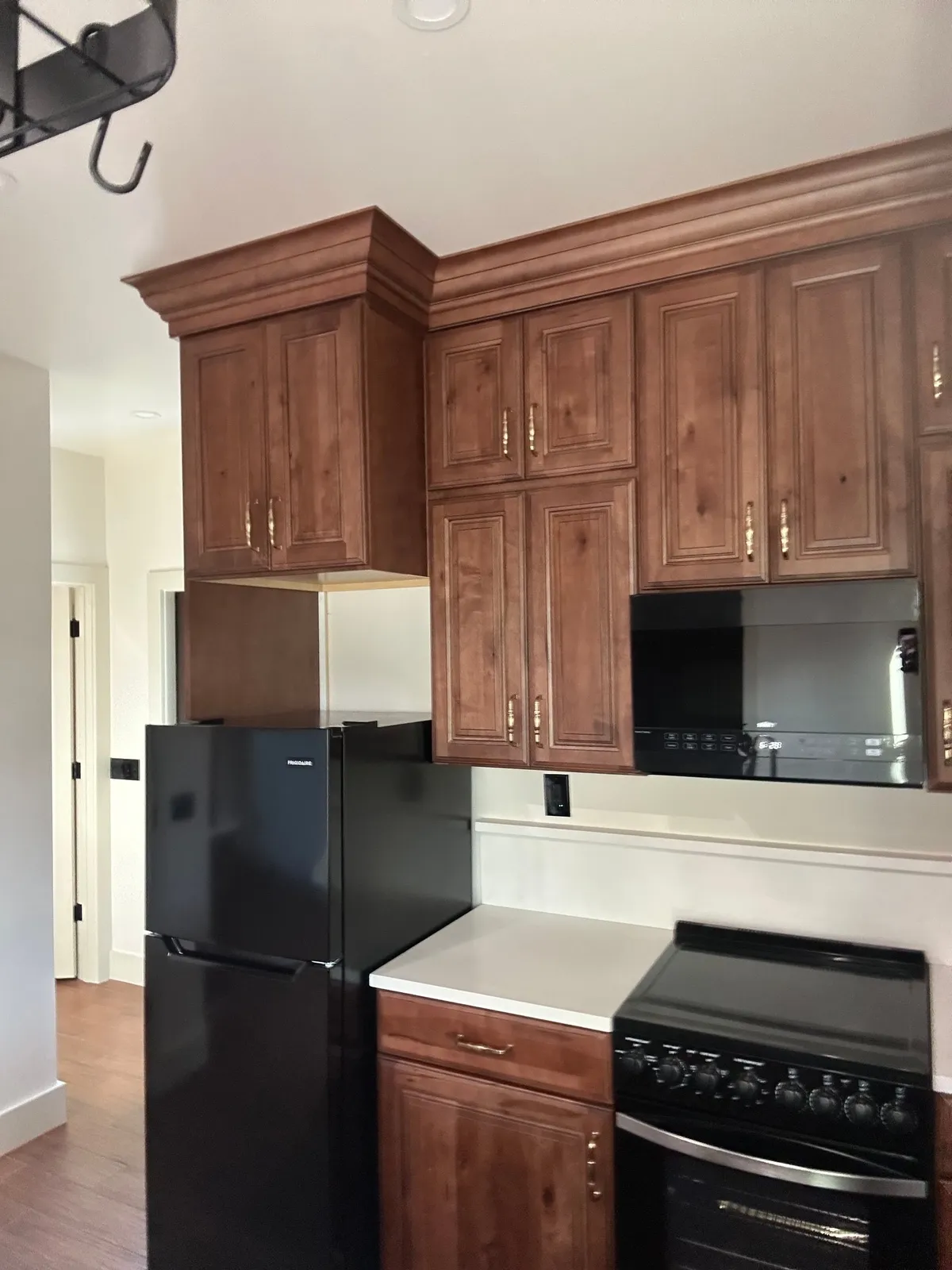 Wood kitchen cabinets with crown molding above a black refrigerator, a range, and a microwave.