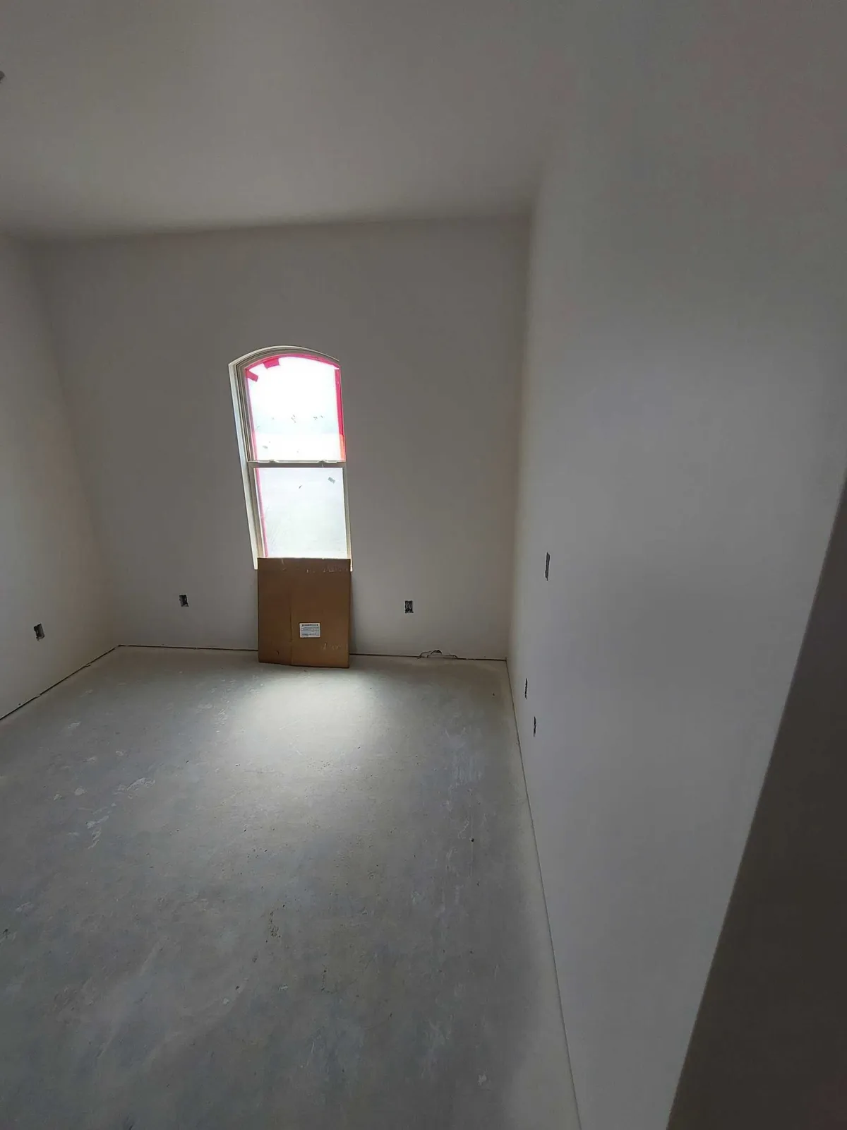 Main room with primed walls and an arched-top window at the far end, before flooring.