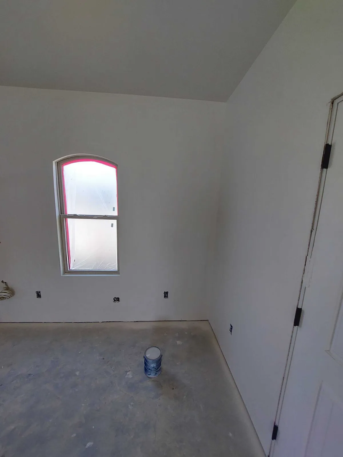 Primed room with an arched-top window and an interior door, before flooring.