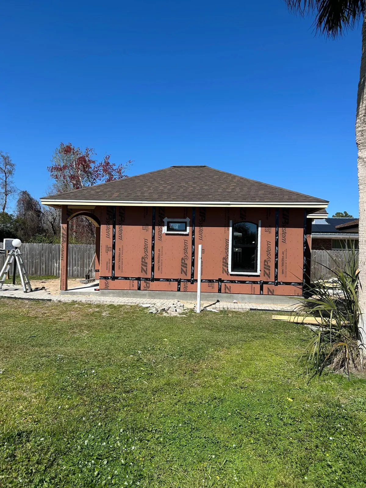 Side of the sheathed studio with windows installed and the roof shingled, seen across the lawn.