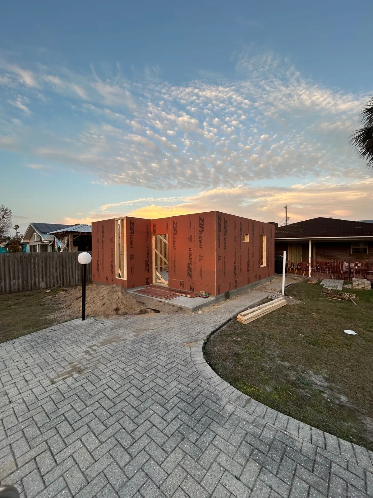 Sheathed exterior walls at sunset, with a curved paver walk leading to the studio.