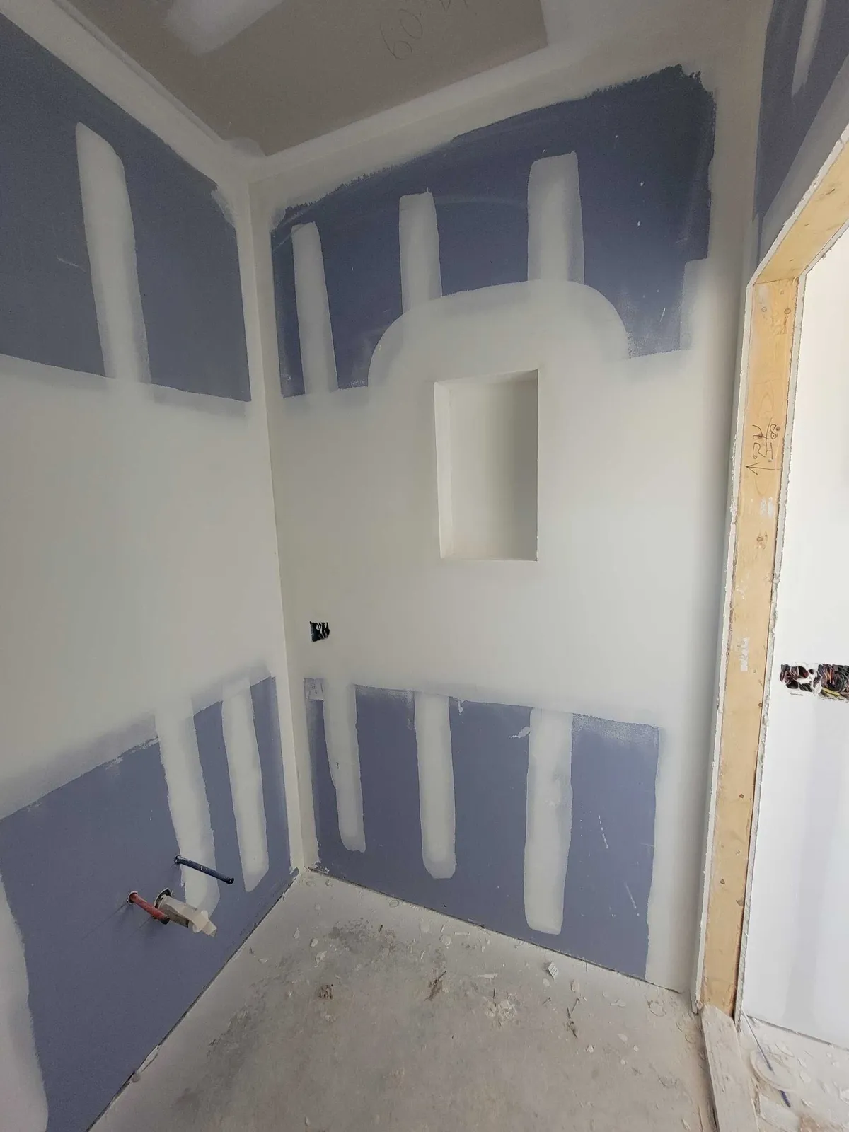 Shower walls with taped board and a recessed niche before tile, beside a framed doorway.