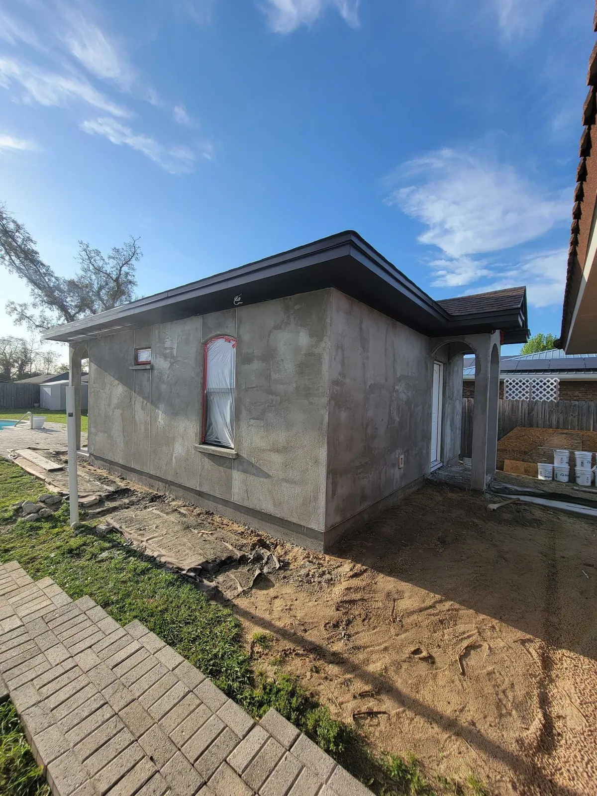 Side wall of the studio after stucco, with an arched-top window and a paver walk in front.