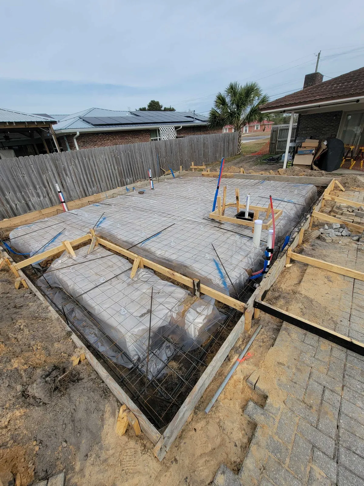 Another view of the formed slab with plastic sheeting, reinforcing mesh, and plumbing stubs, with the porch section in the foreground.