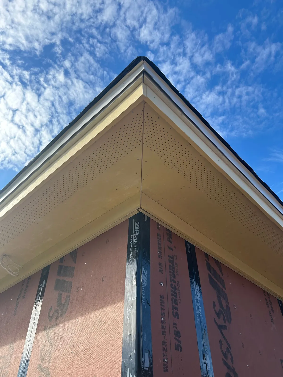 Looking up at a soffit corner where two eaves meet, above the sheathed wall.
