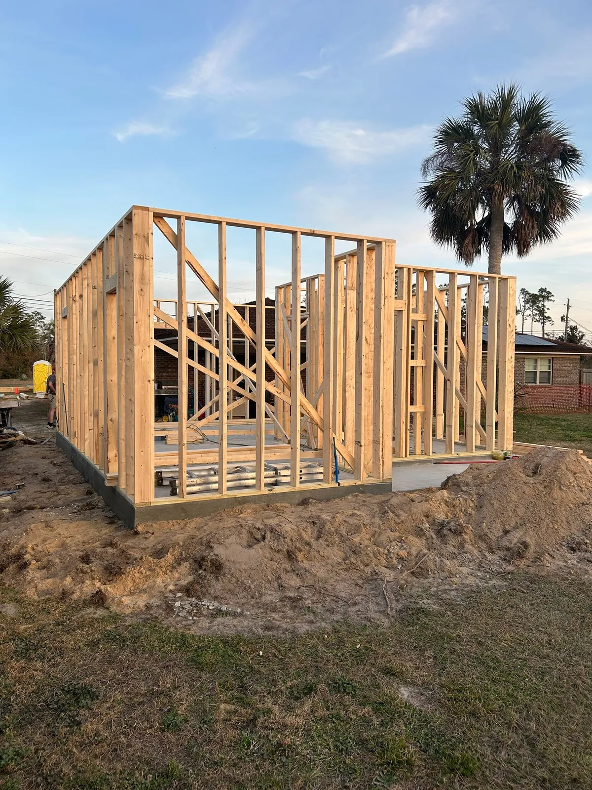 Wood-framed walls standing on the slab, with a palm tree behind.