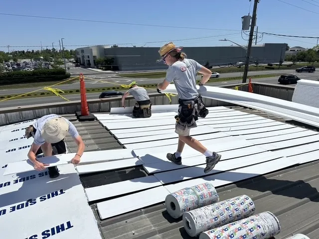 Two Garrett Construction crew members laying roof preparation materials across the metal roof.