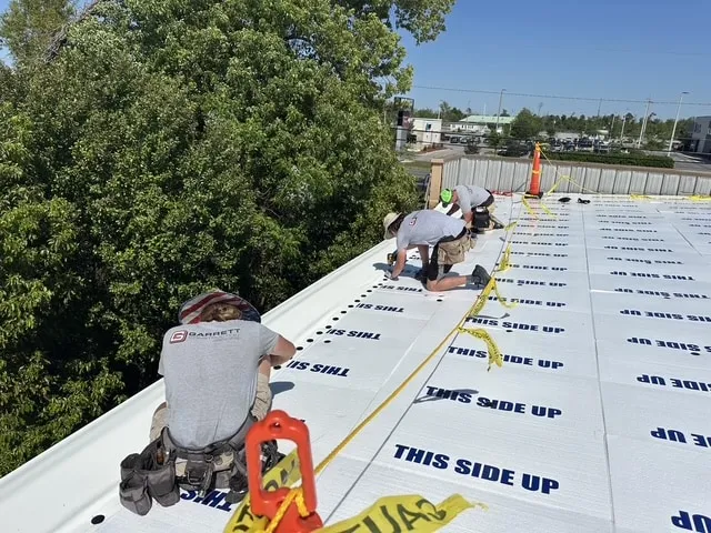 Crew members working along the roof perimeter beside the safety line, with cover board in place.