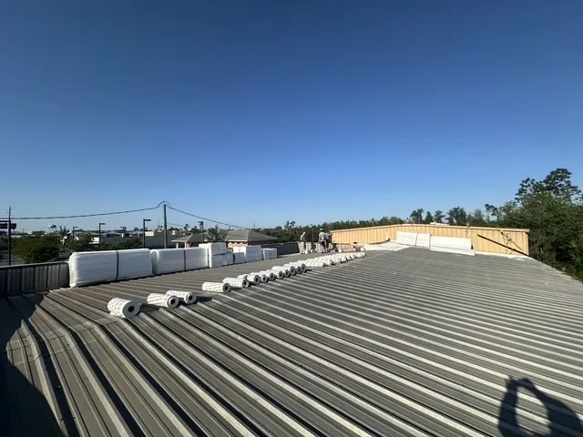 The existing metal roof at the start of the work, with rolls of material staged along the ridge.