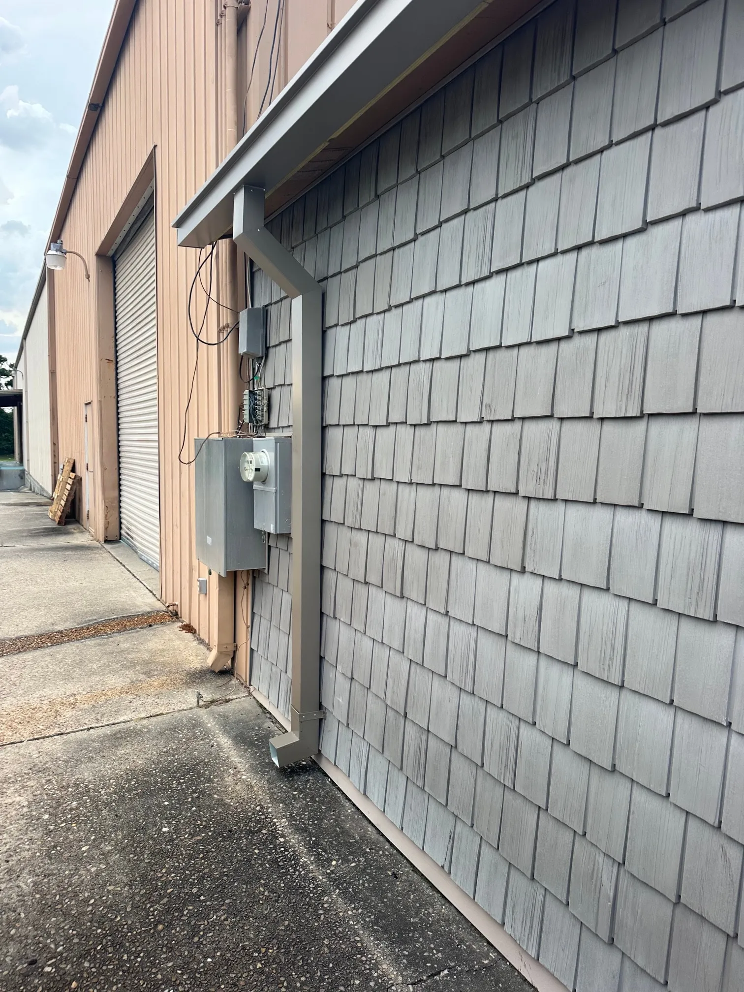 Gutter and downspout installed along the building wall, with the roof edge above.