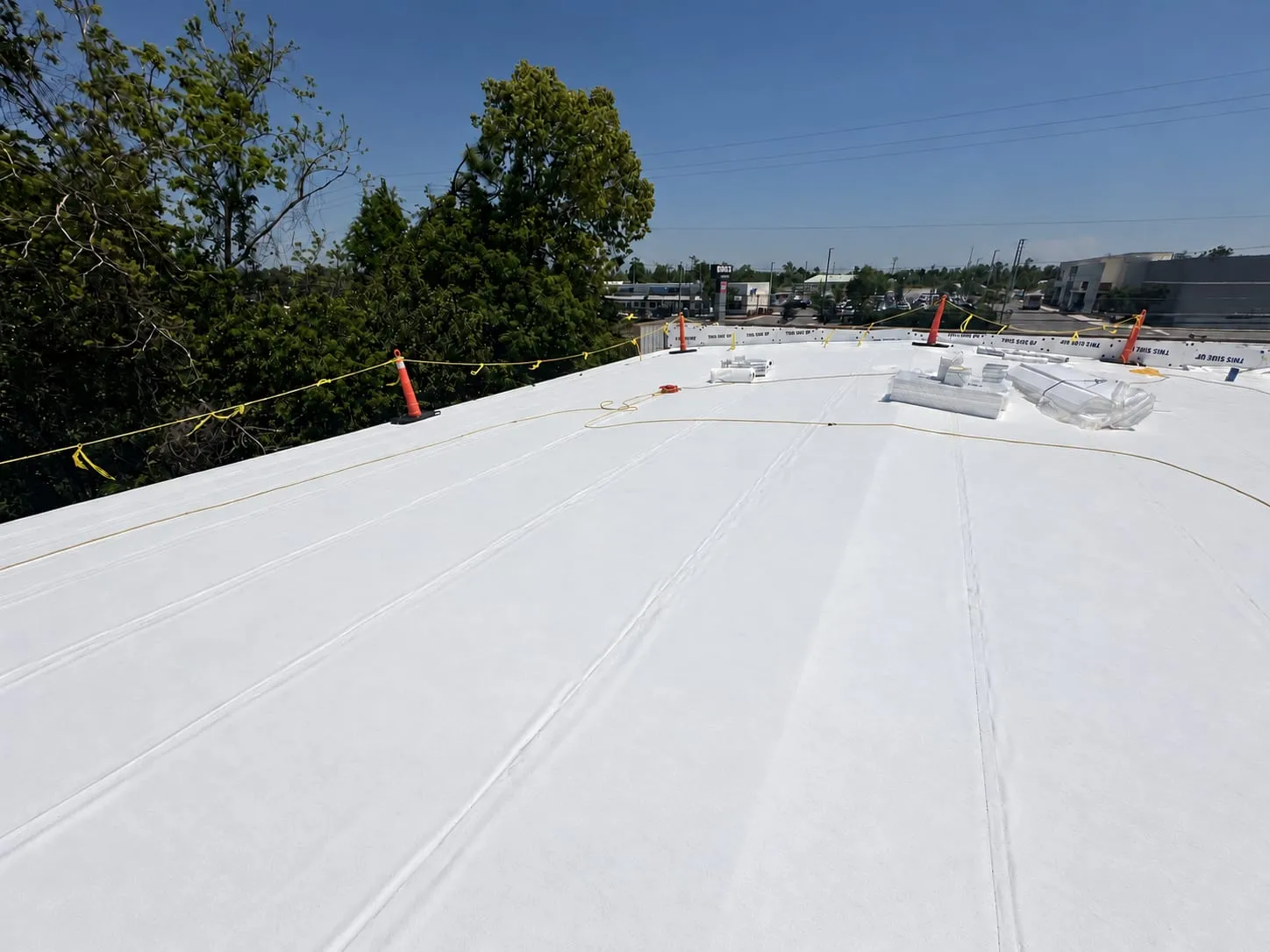 Wide view across the roof with the white membrane laid out, materials on the surface, and safety line along the perimeter.