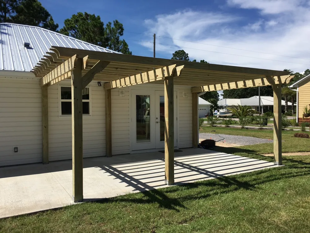 Unfinished wood pergola over a concrete patio beside a light-sided home in Mexico Beach.