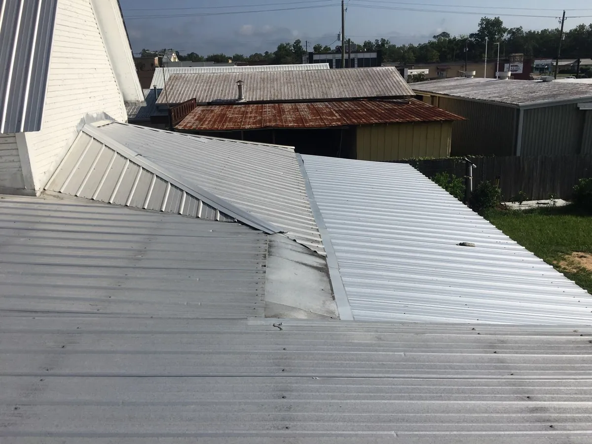Metal roof sections meeting at several junctions beside a wall, with neighboring buildings beyond.