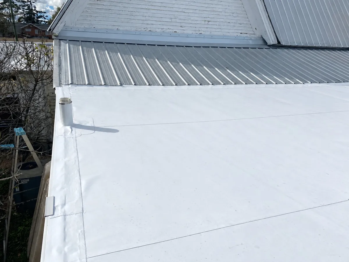 White membrane in the foreground leading to the adjoining metal roof and the house's gable wall.