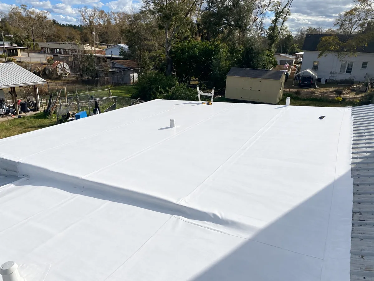 Completed white membrane roof with a vent penetration, overlooking neighboring yards and buildings.
