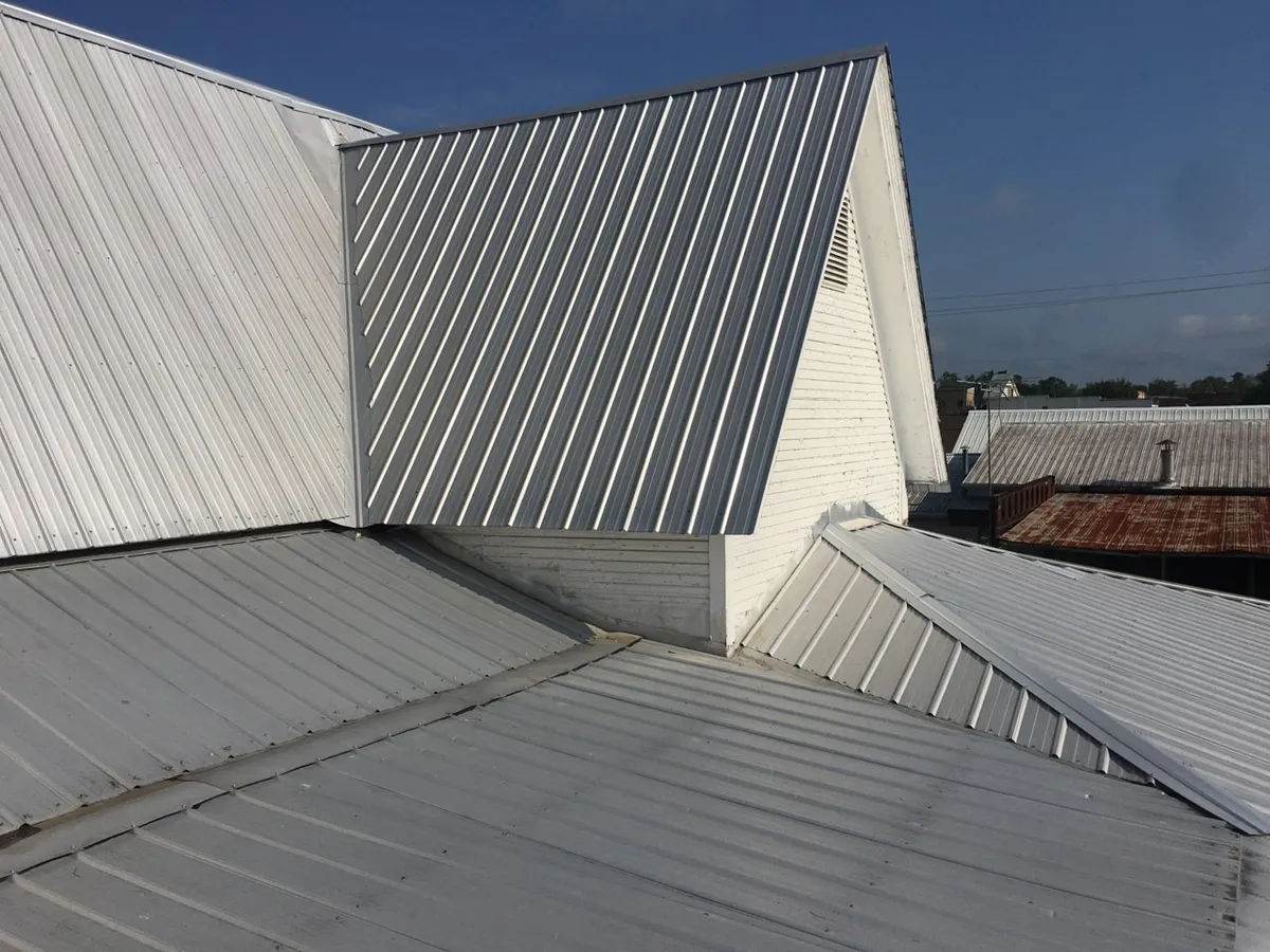 Several metal roof sections meeting below two gables at awkward junctions, before the recover.