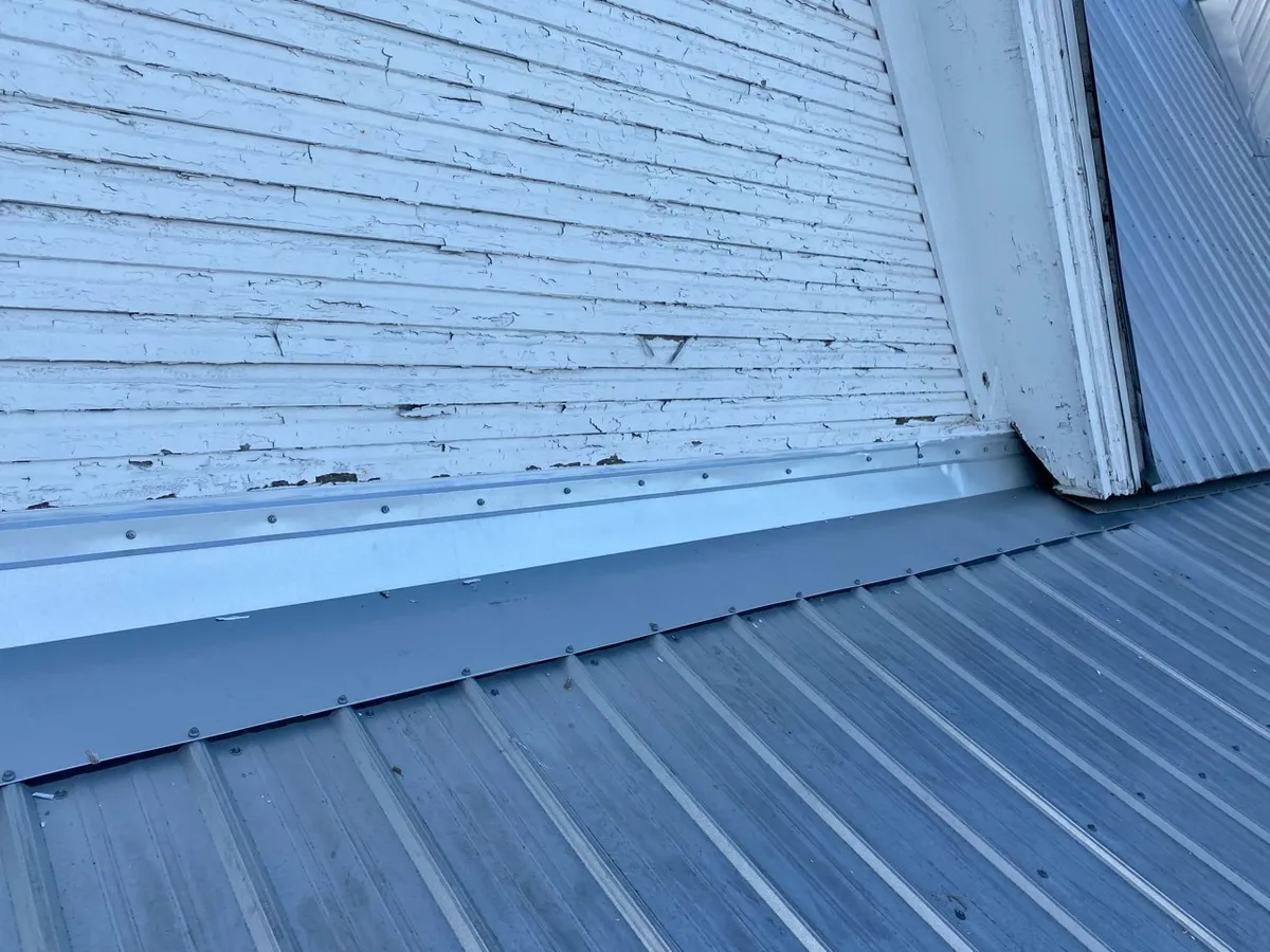 Close view of new metal flashing fastened along the base of a painted wood gable wall, where the metal roof meets it.