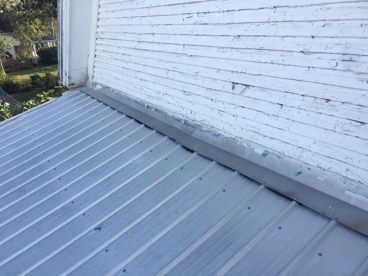 Metal roof meeting a painted wood gable wall along worn metal flashing.