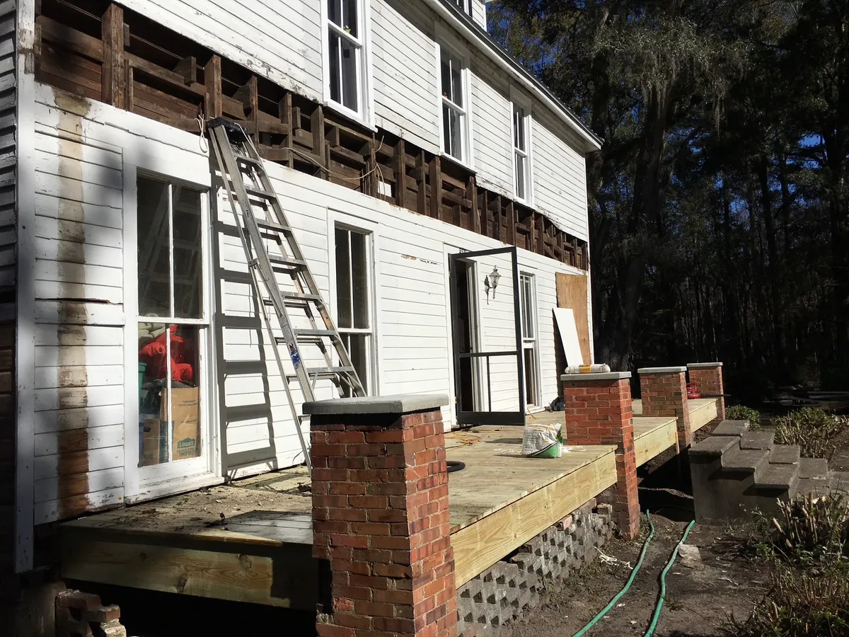 New porch decking along the side of the building, with a band of exposed wall framing above where the siding has been removed.