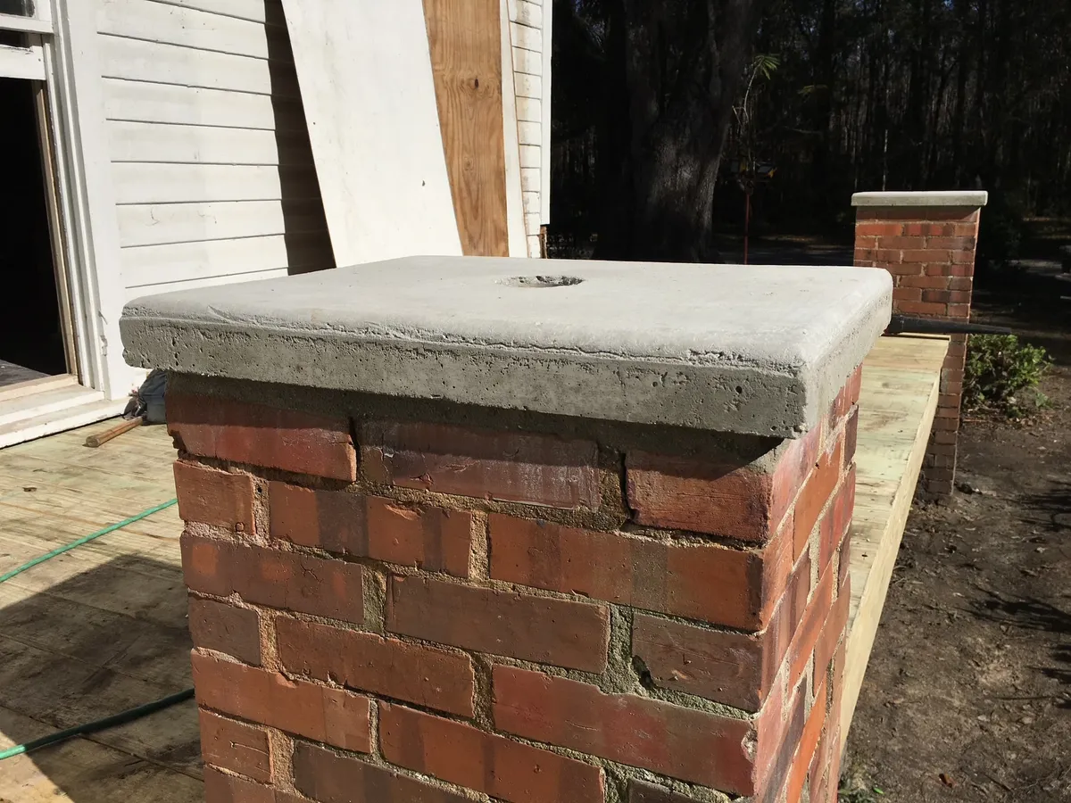 Close view of a brick porch pier with a poured concrete cap overhanging its top, beside the new porch decking.