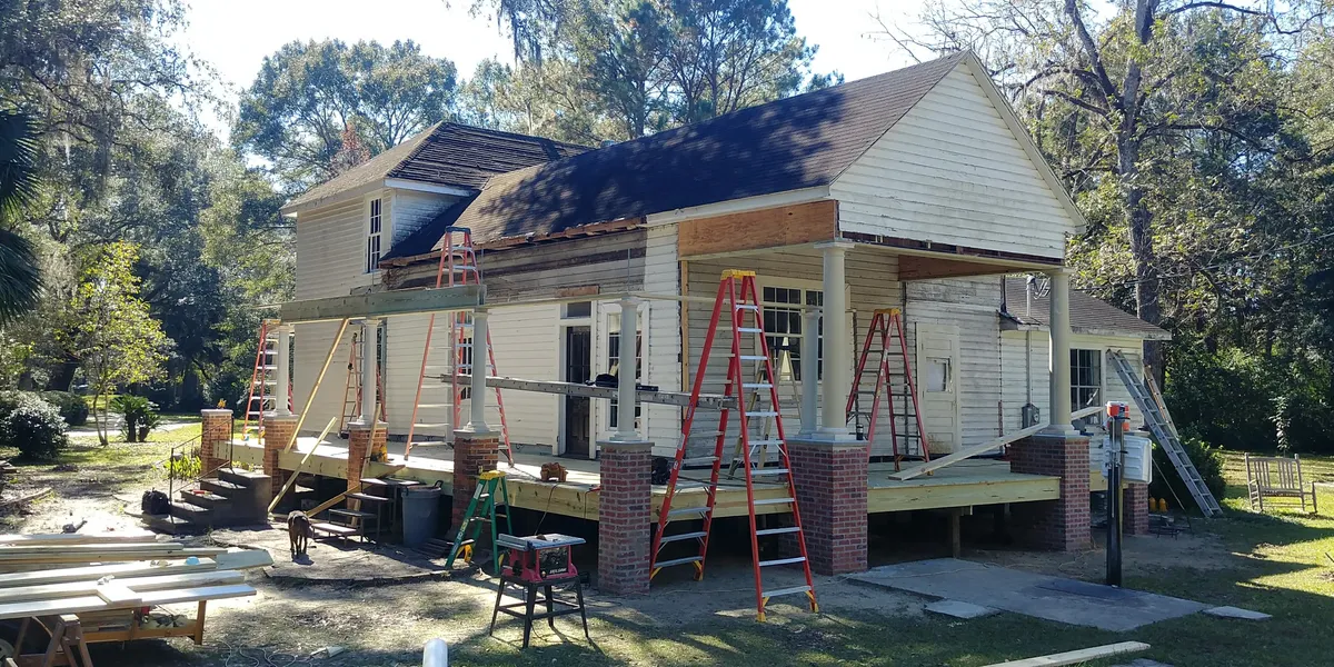 Front of the building with new porch roof framing built above the columns, ladders along the porch, and new decking below.