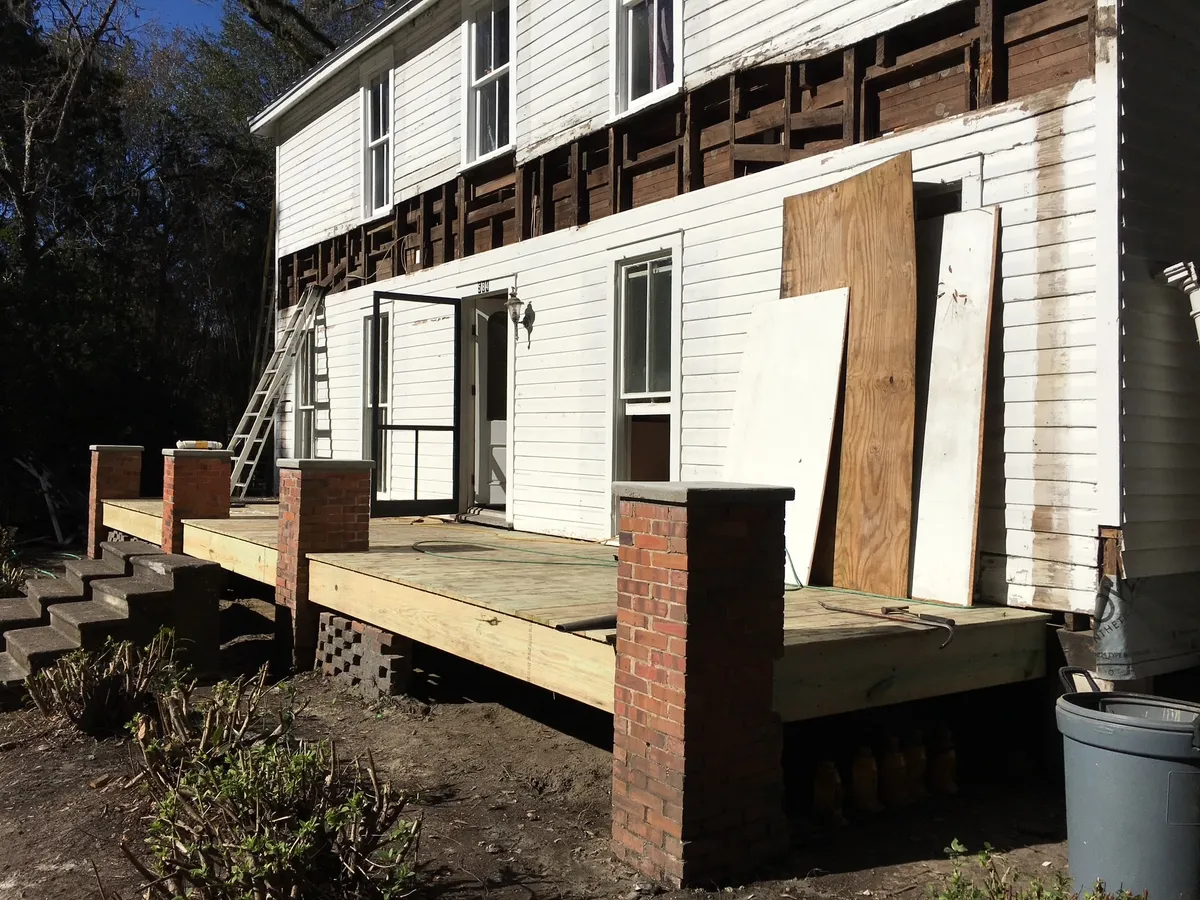 A run of new porch decking on brick piers along the side of the building, with steps at one end and a band of exposed wall framing above.
